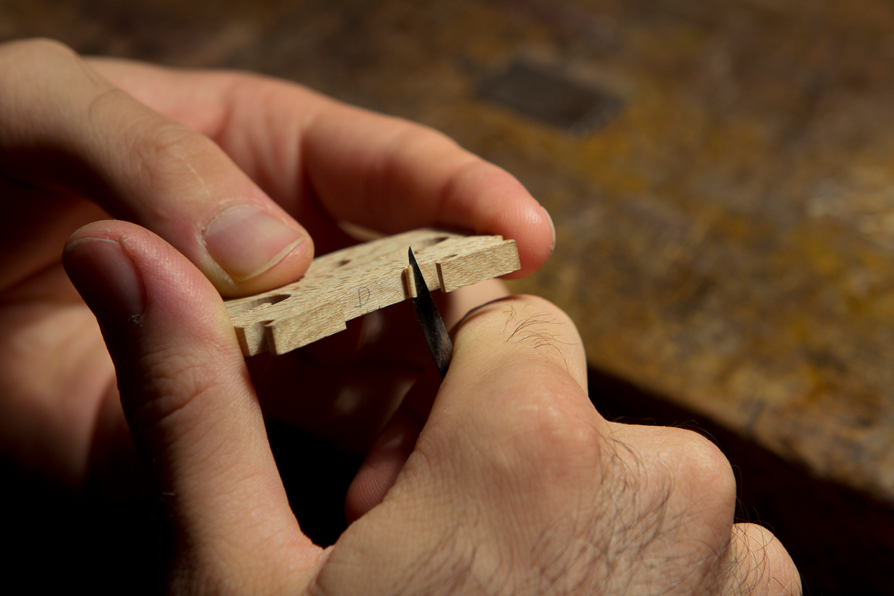 Mão do luthier ajustando o cavalete de um violino com faca